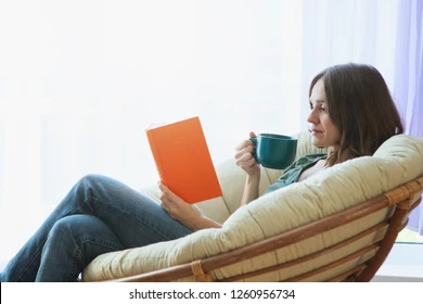 A woman relaxing in a comfortable chair with a book and tea